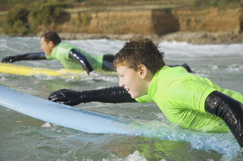 Teenage boy lying on his surfboard paddling - FSIF06681