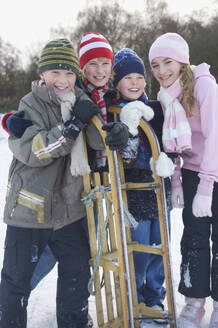 Lächelnde Kinder, die sich auf einen Schlitten stützen - FSIF06682
