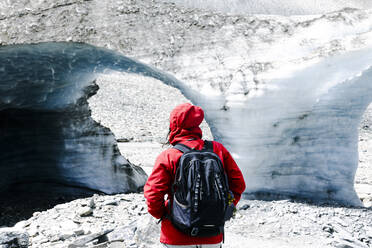 A person in a red jacket observing a massive glacial ice cave formation. - ADSF49183