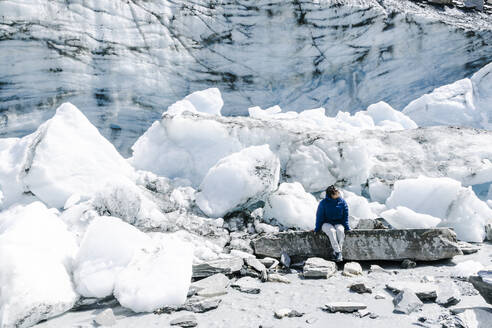 An individual clad in a blue jacket stands among towering ice formations, with the intricate patterns of a glacier wall serving as a backdrop. - ADSF49184