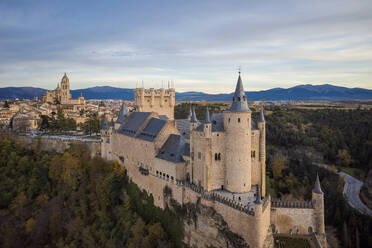 From above aerial view of medieval castle Alcazar of Segovia Spain located on hill with autumn trees next to meandering highway city buildings in sunny daylight - ADSF49190