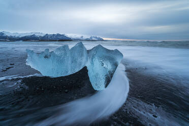 Picturesque scenery of rippling sea water with pieces of broken ice on black sandy beach against cloudy sky in Diamond Beach in Iceland - ADSF49195