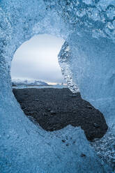 Uneven hole in transparent piece of ice melting in diamond beach in Jokulsarlon in Iceland - ADSF49196