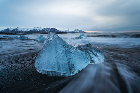 Picturesque scenery of rippling sea water with pieces of broken ice on black sandy beach against cloudy sky in Diamond Beach in Iceland - ADSF49197