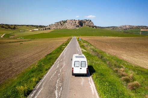 Aerial view of landscape of Andalusia Spain with asphalt road and traveling passenger van towards green meadow with rocky mountains against blue sky - ADSF49239
