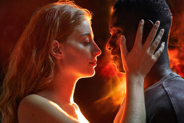 A close-up of a multiracial couple intimately gazing into looking at each other amidst a fiery ambiance in disco - ADSF49250