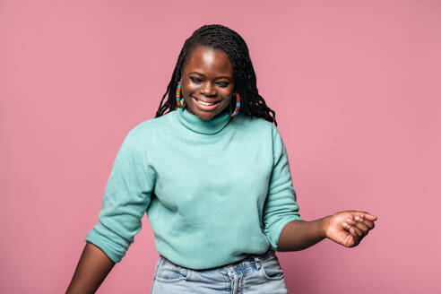 A cheerful African woman in a teal sweater laughs, capturing a moment of genuine happiness against a pink background - ADSF49260