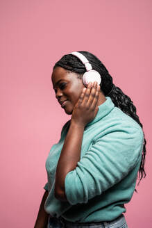 African woman in a serene pose listening to music through her pink headphones, set against a pink backdrop - ADSF49268