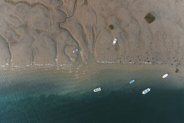 Aerial top view of various boats floating in turquoise ocean near sandy beach on sunny summer day in El Rompido - ADSF49295