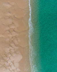 Aerial top view of turquoise ocean washing sandy beach with rippled sand on sunny summer day in El Rompido - ADSF49297