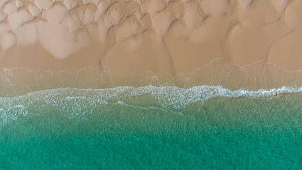 Aerial top view of turquoise ocean washing sandy beach with rippled sand on sunny summer day in El Rompido - ADSF49298