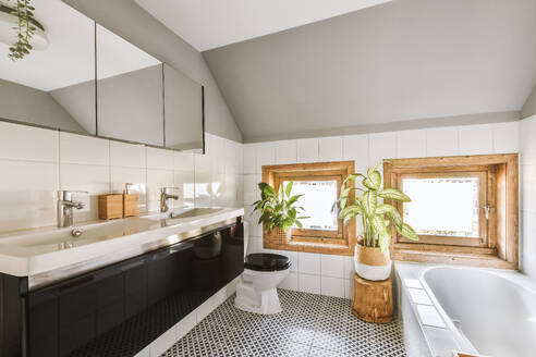 Mirror over ceramic sinks with toilet bowl and bathtub by windows in modern spacious bathroom at home - ADSF49314