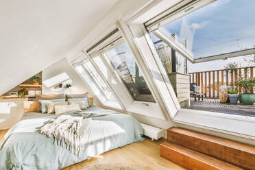 Sunlight falling on comfortable bed through large windows in attic bedroom at contemporary house - ADSF49323
