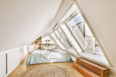 Interior of white attic bedroom with comfortable bed and large bright windows in modern apartment - ADSF49324
