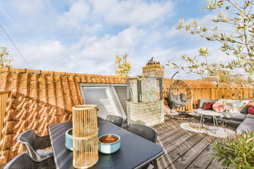 Dining table with comfortable couch and swing chair arranged in balcony outside loft house under cloudy sky - ADSF49325