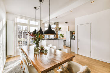 Interior of dining room with pendant lights hanging over dining table and chairs against window and kitchen - ADSF49330