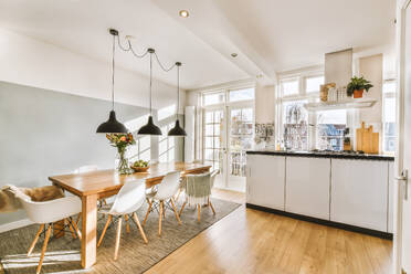 Pendant lights hanging over dining table and chairs in front of open kitchen by window in contemporary apartment - ADSF49331