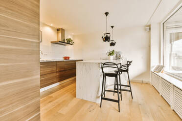 Kettle shaped lamps hanging over marble island and bar stools in spacious modern kitchen at home - ADSF49337