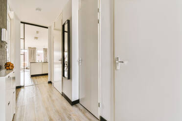 Narrow hallway with doors of different rooms and mirror on white wall in contemporary apartment - ADSF49339