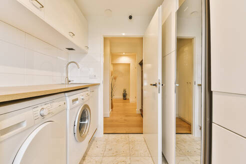 Washing and dryer machines under wooden counter in kitchen with open door leading to hallway at modern apartment - ADSF49344