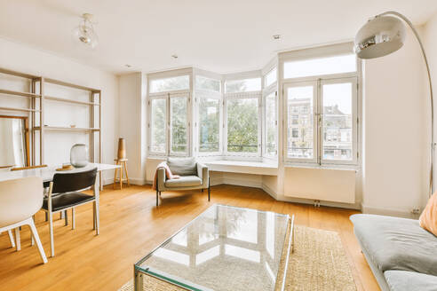 Interior of spacious living room with couch and glass coffee table against bay window in contemporary white apartment - ADSF49355