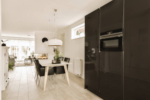 Dining table and chairs arranged by black refrigerator and microwave in modern kitchen at contemporary home - ADSF49368