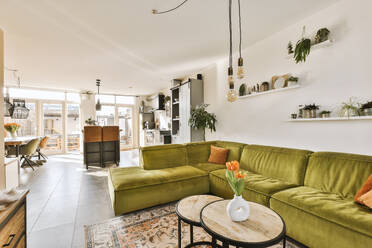 Green couch with coffee table and light bulbs arranged in living room against open plan kitchen in contemporary apartment - ADSF49370