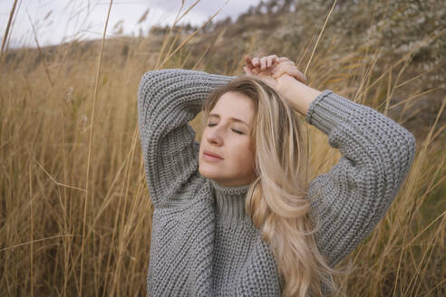 Blonde Frau mit grauem Pullover in der Nähe von trockenem hohem Gras - YBF00311