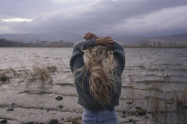 Blonde Frau mit erhobenen Armen steht vor einem See bei Sonnenuntergang - YBF00313