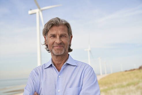 Smiling senior businessman in front of wind turbines - PHDF00094