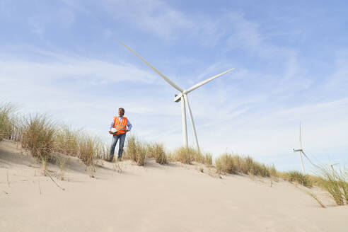 Ingenieur steht in der Nähe von Windturbinen auf einer Sanddüne - PHDF00096