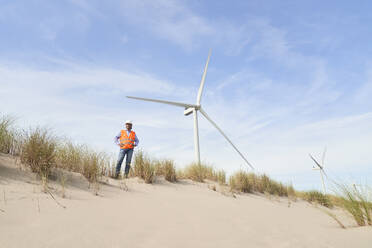 Ein leitender Ingenieur steht in der Nähe von Windkraftanlagen auf einer Sanddüne - PHDF00097