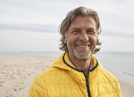 Glücklicher Mann mit gelber Jacke am Strand - PHDF00126