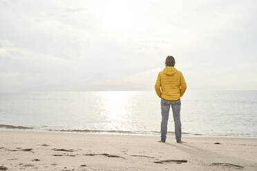 Mann mit Händen in den Taschen steht in der Nähe von Meer am Strand - PHDF00127