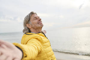 Lächelnder älterer Mann mit ausgestreckten Armen am Strand stehend - PHDF00130