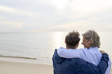 Glücklicher Vater und Sohn mit Arm um einander am Strand - PHDF00133