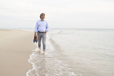 Älterer Mann mit Schuhen und Spaziergang an der Küste am Strand - PHDF00136