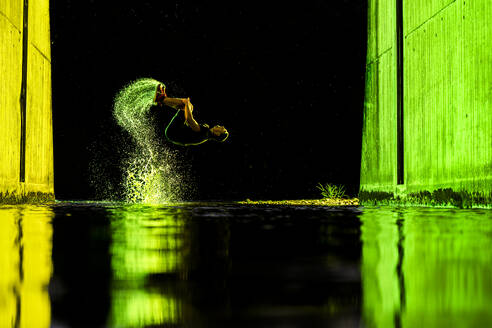 Young man backflipping with water under bridge at night - STSF03792
