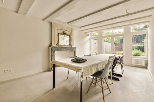 Interior of dining room with table and chairs arranged next to large bright window in modern apartment with white walls - ADSF49394