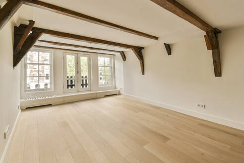 Interior of empty living room with parquet floor and wooden beams on ceiling in unfurnished apartment with windows and white walls - ADSF49397