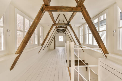 Interior of long empty hallway with wooden beams and windows surrounded with white walls in modern house - ADSF49400