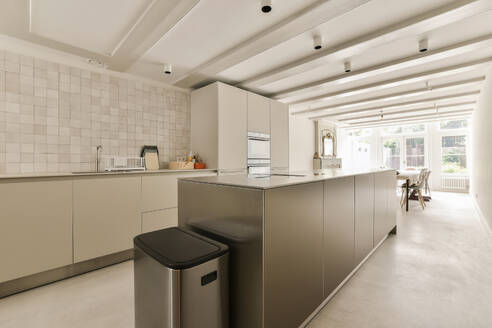 Interior of renovated kitchen with large island and white cabinets against window in contemporary apartment - ADSF49401
