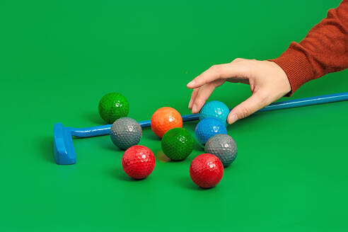 Crop hand putting ball into mini golf set on green surface in studio with golf stick and with various balls - ADSF49428