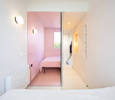 A modern living space featuring a gray sofa, wooden cabinetry, and an archway leading to a pink room. - ADSF49441