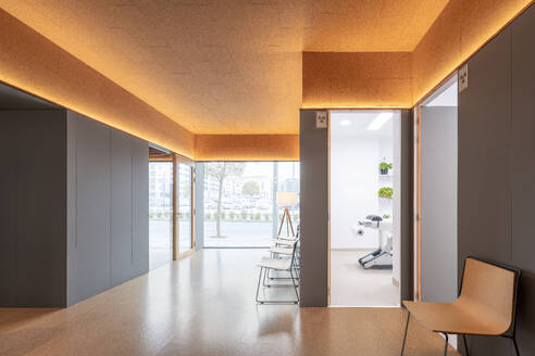 Bright and airy waiting area in a dental clinic with cork ceiling and minimalist chairs against large glass windows with city view - ADSF49443