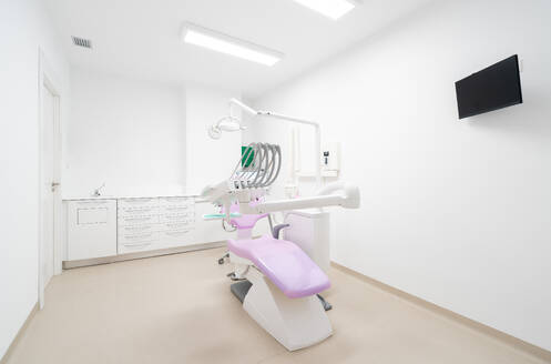 White dental chair with modern equipment placed in spacious office with cabinets and various tools in contemporary dentistry - ADSF49444