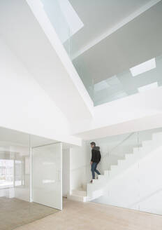 Modern architectural design of an interior space with a person ascending a glass staircase - ADSF49446