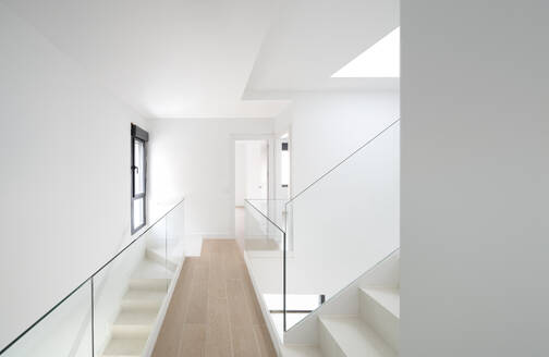 Bright interior hallway with modern design, featuring a staircase, glass railing, and a skylight - ADSF49450