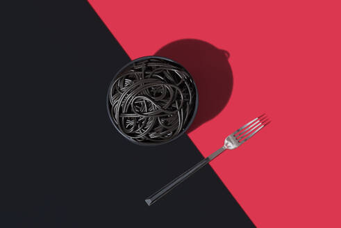 Top view of black spaghetti in a bowl placed on black and red background near fork - ADSF49459