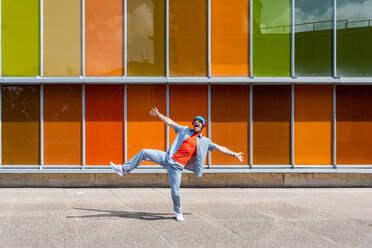 Joyful man dancing energetically in front of a multicolored windowed building - ADSF49494